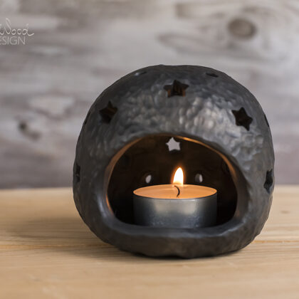 Black pottery candle holder with holes in shape of stars.