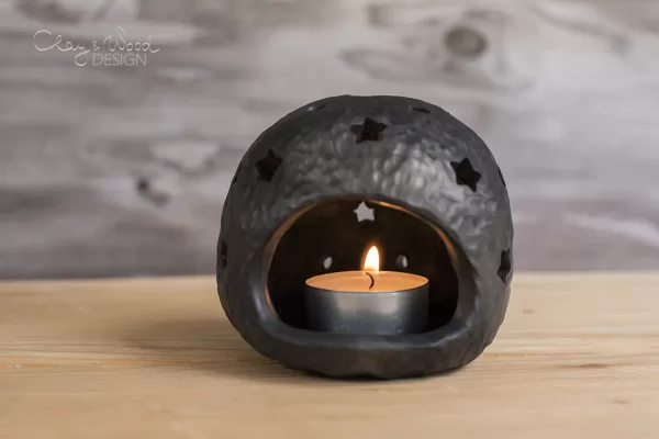 Black pottery candle holder with holes in shape of stars.